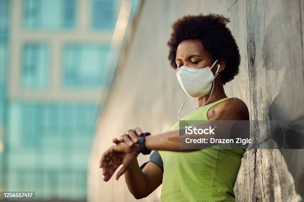 African American Female Runner With Face Mask Using Fitness Tracker Outdoors Stock Photo - Download Image Now
