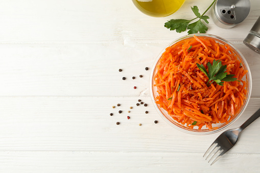 Composition with tasty carrot salad on white wooden background. Korean carrot