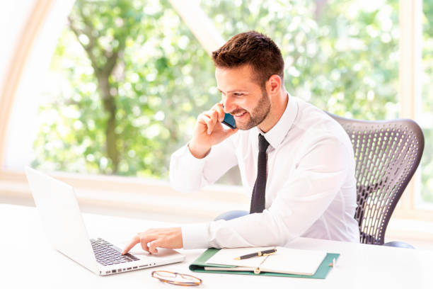 istock Happy businessman using laptop and mobile phone while working in the office 1256560322