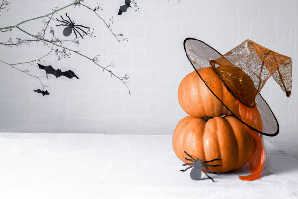 istock Pumpkins with a witch hat and a paper spider DIY on a white background with a brunch with bats. Minimal Halloween card 1256562145