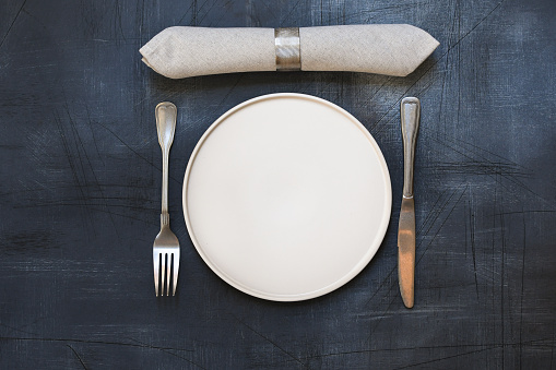 White craft plate, cutlery and napkin on dark stone table. Top view, copy space, Table setting. background for menu, layout, place for text , recipe background
