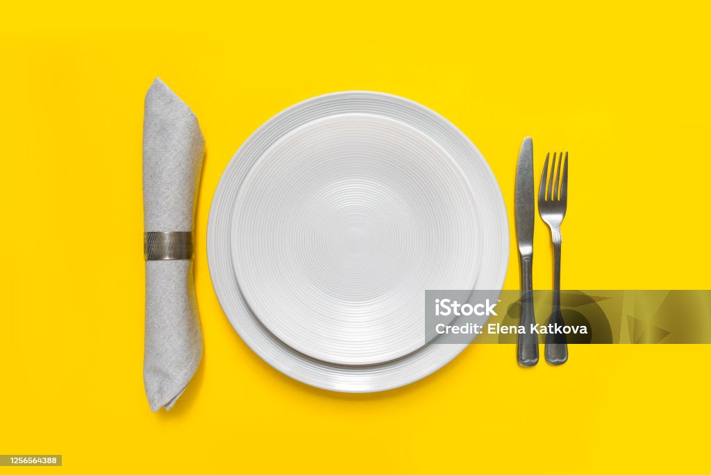 White plate on yellow background White craft plate, cutlery and napkin on yellow background isolate. Top view, copy space, Table setting. background for menu, layout, place for text. concept of food delivery from a restaurant Setting The Table Stock Photo