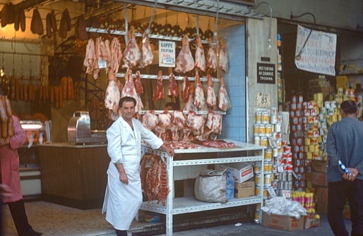 Athens Attica, Greece, 1975. Butcher shop with open display in Athens. Also: seller and passers-by.