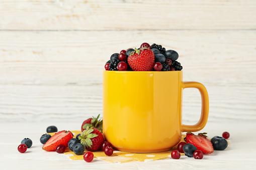 Composition with cup of fresh berries on white wooden background
