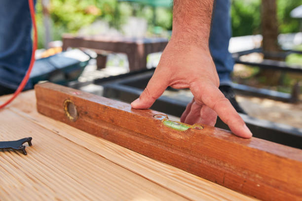 Unrecognizable skilled senior carpenter working in a back yard, on a construction site with a wooden level tool.