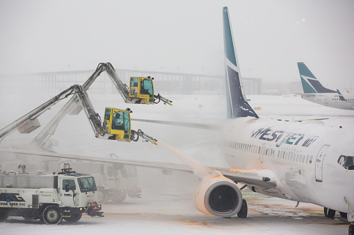 Calgary, Alberta, Canada-November 9, 2012: West Jet 737 passenger gets de-iced at Calgary International Airport (YYC) by ground crews during a heavy winter storm. A de-icing spray of heated solvents and steam blasts the wings of the jet before takeoff. Shot in the morning of November 9, 2012.