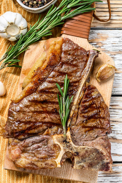 istock Grilled T bone steak on a chopping Board. Cooked tbone beef. White wooden background. Top view 1256574794