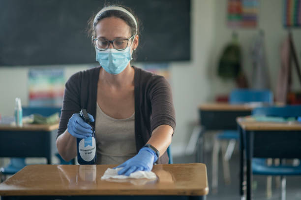 istock Teacher sanitizes desk 1256576773
