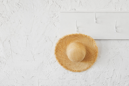 Tropical wicker hat on a white wooden hanger in a minimalistic interior. Travel delayed during the coronavirus epidemic.