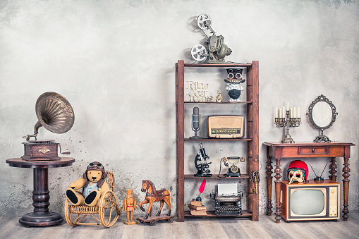 Still life with antique gramophone, old Teddy Bear, toy horse, collection of outdated media devices and writers tools, microscope, desk mirror front concrete background. Vintage style filtered photo
