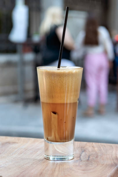 A greek cold coffee, freddo cappuccino placed on a wooden table outdoors. A greek cold coffee, freddo cappuccino placed on a wooden table outdoors, urban background. freddo cappuccino stock pictures, royalty-free photos & images