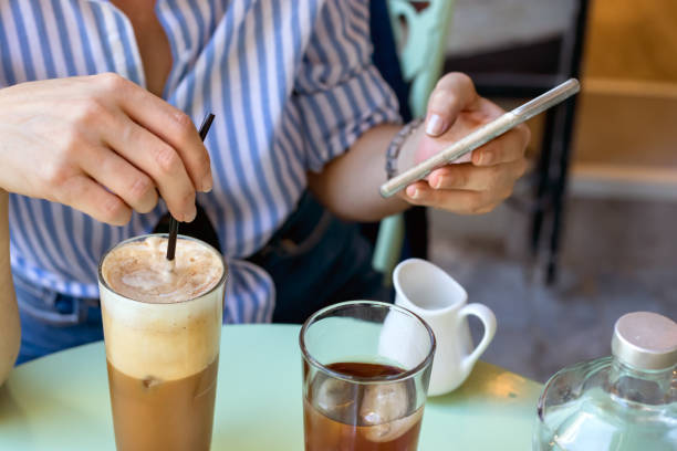 Female hand stirring a straw on a greek cold coffee, freddo cappuccino, outdoors Female hand stirring a straw on a greek cold coffee, freddo cappuccino while looking a mobile, coffee break concept. freddo cappuccino stock pictures, royalty-free photos & images