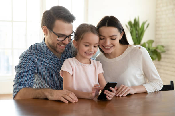 istock Smiling mother and father with little daughter using smartphone together 1256590489