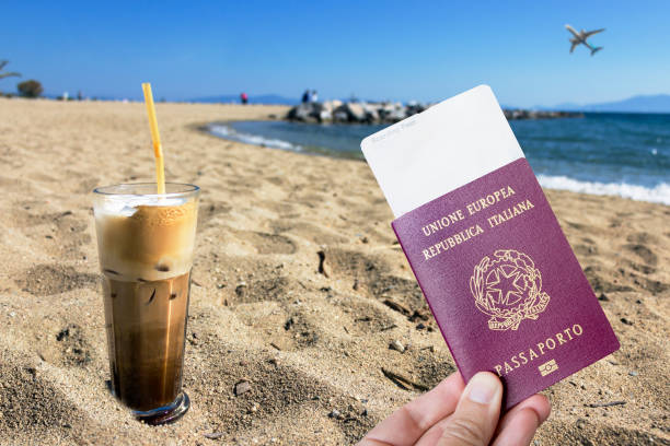 male hand holding an european passport with a covid-19 immunity certificate over a frape coffee on the beach. - photography starbucks flag sign imagens e fotografias de stock