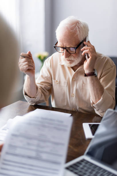 istock Selective focus of man talking on smartphone near papers and gadgets on table 1256595926