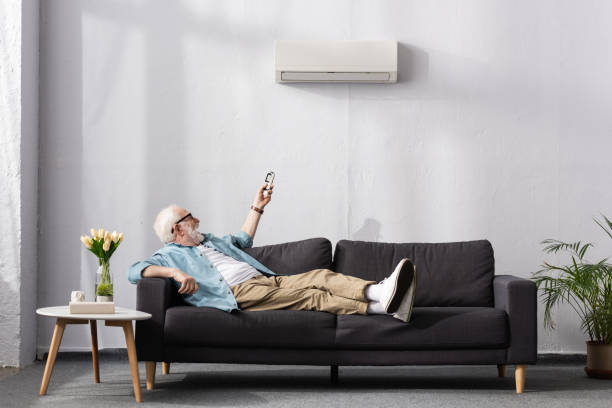 istock Cheerful senior man using remote controller of air conditioner while sitting on couch 1256595940