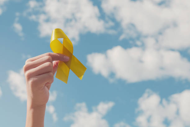 mani che tengono il nastro d'oro giallo sul cielo blu, sarcoma awareness, cancro osseo, consapevolezza del cancro infantile, giallo settembre, concetto di giornata mondiale della prevenzione del suicidio - suicidio foto e immagini stock