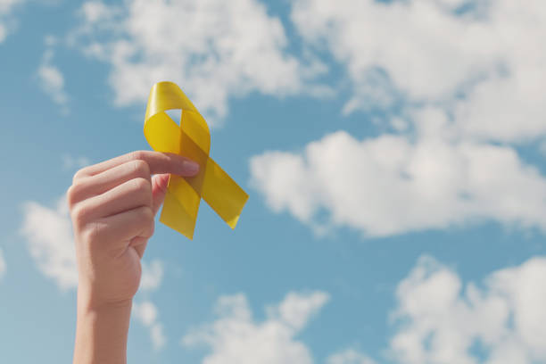Hands holding yellow gold ribbon over blue sky, Sarcoma Awareness, Bone cancer, childhood cancer awareness, September yellow, World Suicide Prevention Day concept Hands holding yellow gold ribbon over blue sky, Sarcoma Awareness, Bone cancer, childhood cancer awareness, September yellow, World Suicide Prevention Day concept suicide photos stock pictures, royalty-free photos & images