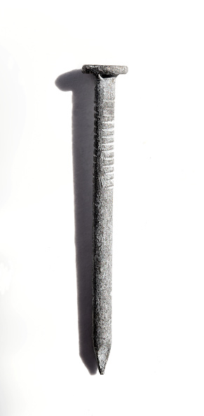 A Single Nail on white surface with shadow imaged from side.