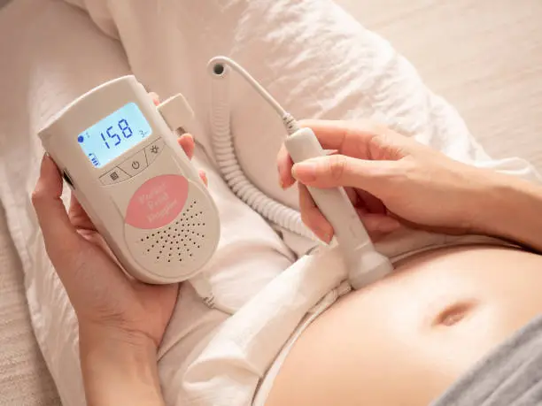 Photo of asian woman using pocket fetal doppler to monitor baby heart beat. expectant mother happy and smile when examine belly.