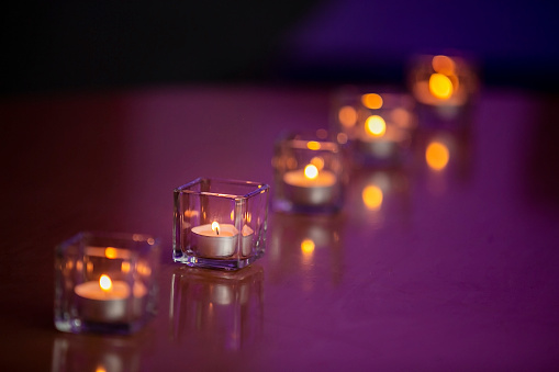 Lit tealight candles in glass containers on a glossy table top with a purple tint background