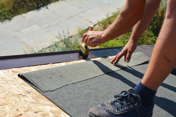 a building contractor is installing underlayment, a layer of bitumen tape on sheathing for overall roof protection at the ridge of the rooftop on the house construction, repairing. - bitumen felt imagens e fotografias de stock