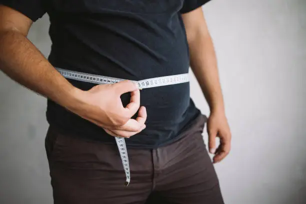 Overweight man measuring waist with measure tape, close up image. Weight loss, motivation, fat burning