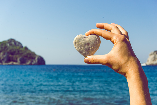 A woman hand holding a heart shaped stone on the beach