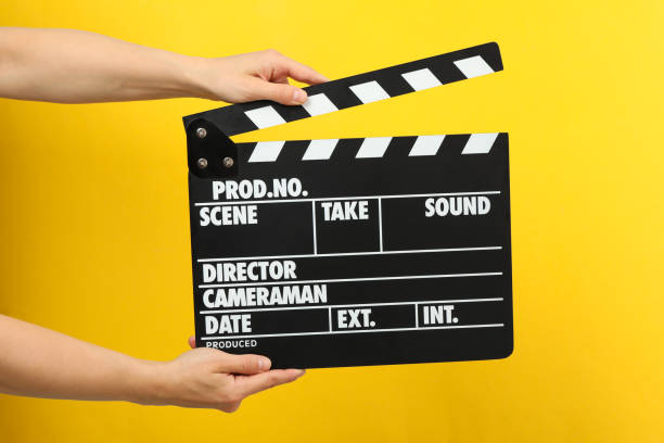 istock Female hands holding clapper board on yellow background 1256622187