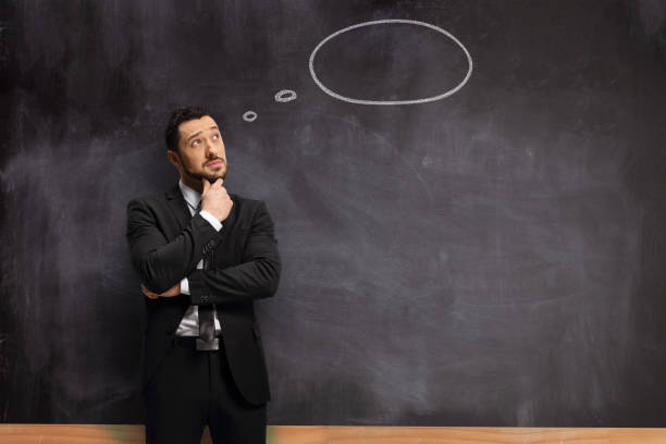 istock Man in a suit standing in front of a blackboard with a thought bubble 1256627967