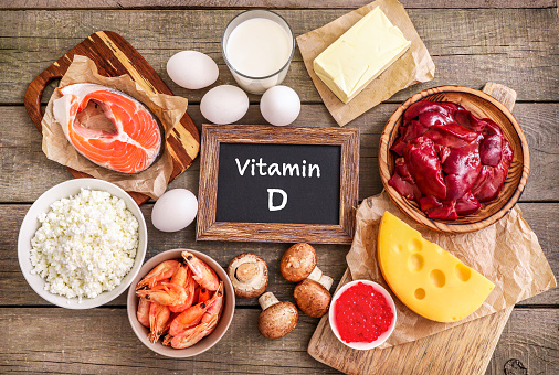 Assortment of high vitamin D sources on wooden background: milk, liver, prawns, salmon, cheese, butter, red caviar, eggs, mushrooms, cottage cheese. Top view.
