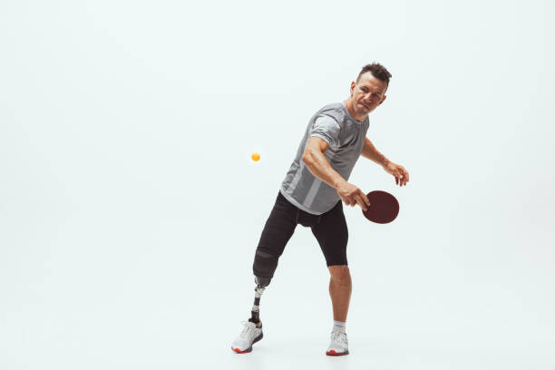 istock Athlete with disabilities or amputee isolated on white studio background. Professional male table tennis player with leg prosthesis training and practicing in studio. 1256634596