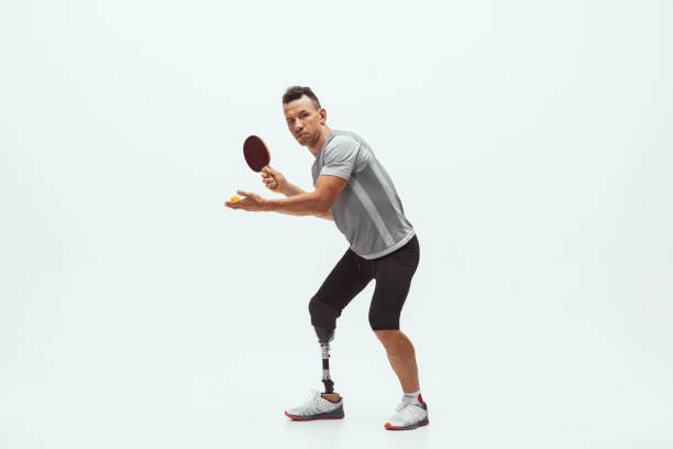 Athlete with disabilities or amputee isolated on white studio background. Professional male table tennis player with leg prosthesis training in studio. Disabled sport and healthy lifestyle concept.