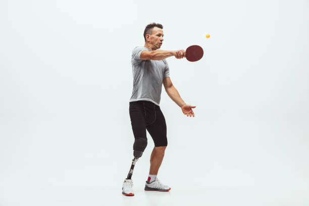 istock Athlete with disabilities or amputee isolated on white studio background. Professional male table tennis player with leg prosthesis training and practicing in studio. 1256634619