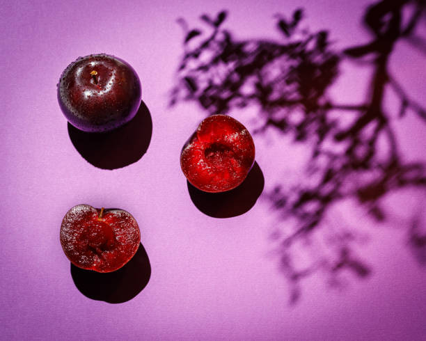 still life with plums on color background and tree shadow