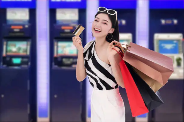 young happy woman holdking shopping bag and withdrawing money from credit card at ATM