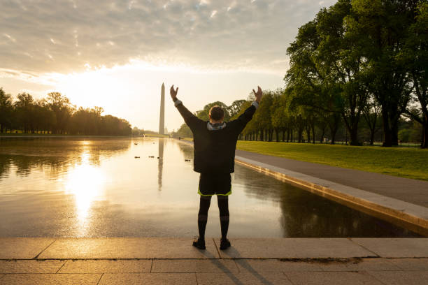 A man with arms outstretched with the view of reflecting pool and Washington Monument in background, Sunrise in Washington DC A man with arms outstretched with the view of reflecting pool and Washington Monument in background, Sunrise in Washington DC washington monument reflecting pool stock pictures, royalty-free photos & images