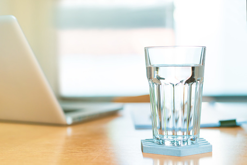 Drinking water in a glass on the wooden table, working from home with healthcare and working life balance concept with copyspace.