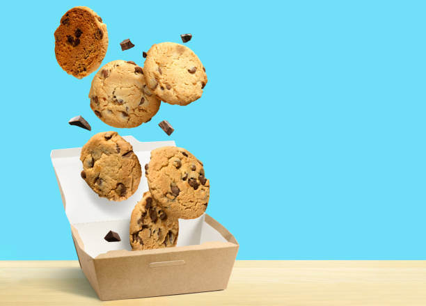 schokoladen-chip-cookies fallen in papier-box über aquablauen hintergrund. - drop cookies stock-fotos und bilder