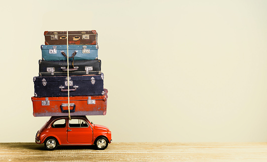 Vintage worn suitcases on retro toy car roof creative travel concept. Copy space