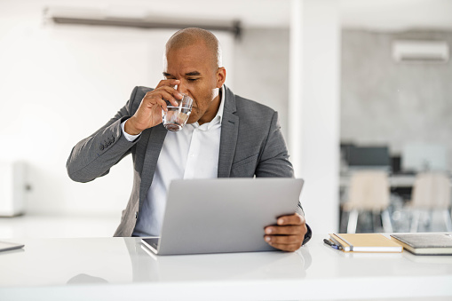 Mid adult black businessman drinking fresh water while working on a computer in the office.