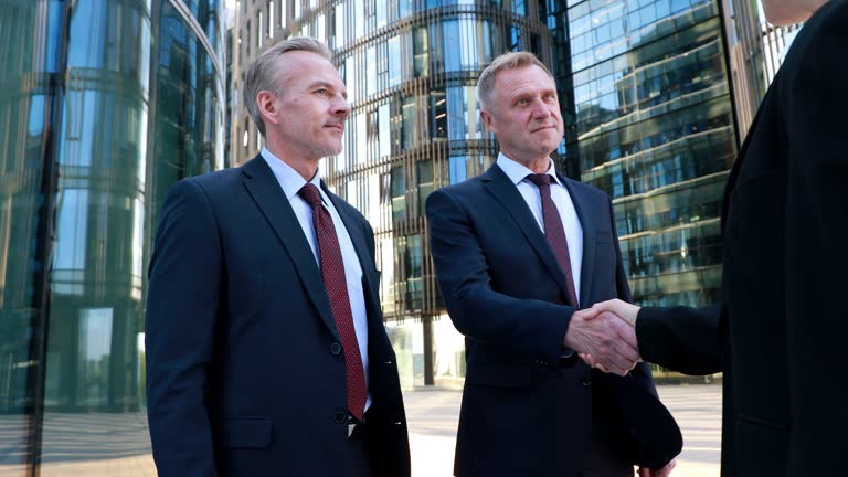 Invitation to business team looking at camera three business partners do handshake in front skyscrapers. A good business deal