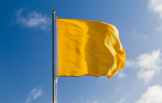 Yellow warning flag on a beach lifeguard station waving on strong wind above blue sky