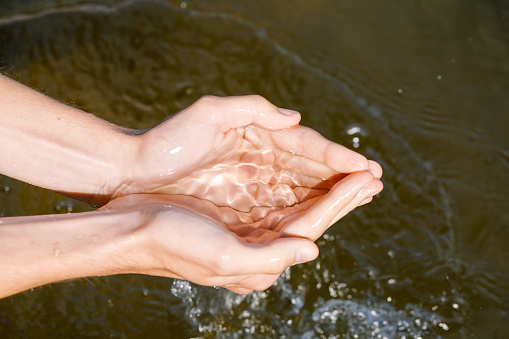 Woman taking raw unfiltered water from a natural source by cupped hands