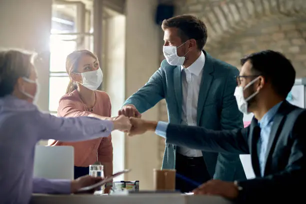 Photo of United business team with face masks colliding their fists on a meeting in the office.