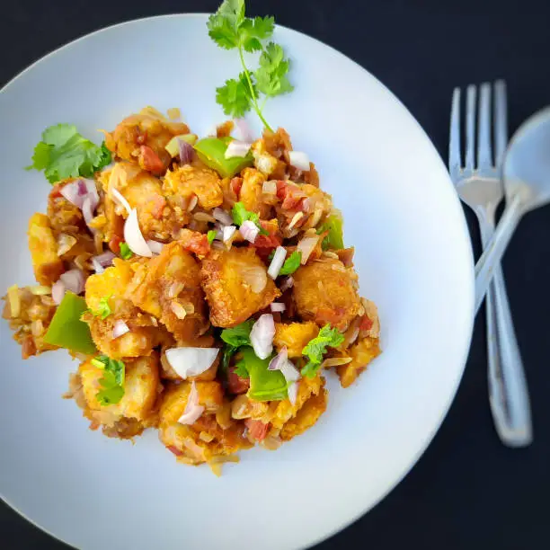 Photo of Indian style bread Manchurian prepared with capsicum and onion spreaded on it and plated beautifully in white plate with spoons