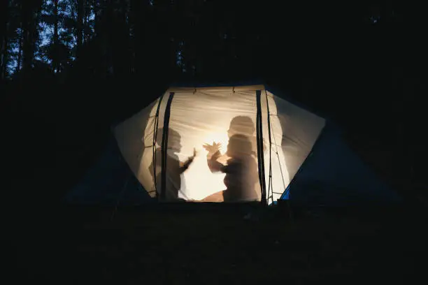 Photo of Children making shadow puppets in a camping tent at night