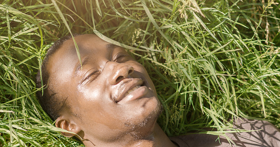 Happy african american guy lying on green grass, enjoying summer sun, close up, free space