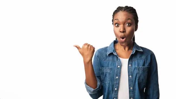 Photo of Shocked African Girl Pointing Thumb At Free Space, Studio Shot