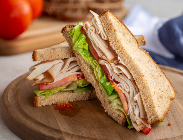 Turkey Sandwich With Tomato and Lettuce Healthy sandwich with turkey, tomato and lettuce on whole wheat bread on a wooden board turkey meat stock pictures, royalty-free photos & images